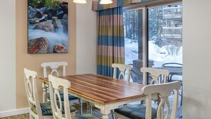 A dining area with a wooden table and white chairs, a painting of a waterfall, and a view of a snowy landscape through a window. - Charming Lodge-Style Resort with Something to do in Every Season! (Zephyr Cove)