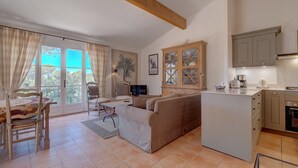 A living room with a sofa, a dining table, and a kitchen area with cabinets and a coffee maker. - 3-BEDROOM TOWNHOUSE WITH GARDEN (N°411) (La Motte)