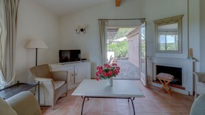 A living room with a television, a white table with a vase of flowers, a fireplace, and a view of the outside. - 3-BEDROOM TOWNHOUSE WITH GARDEN (N°412) (La Motte)