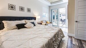 Un dormitorio amplio con una cama grande, cabecera oscura y vistas al patio exterior a través de una puerta corrediza de vidrio.
