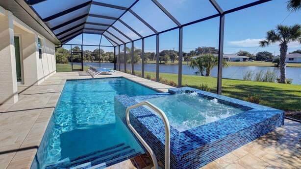 Piscina con cerramiento de vidrio, jacuzzi y vista a un lago y palmeras.