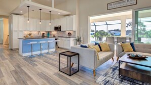 Una cocina moderna con armarios blancos, una isla azul con taburetes altos e iluminación colgante.