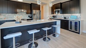 Une cuisine moderne avec des meubles de couleur sombre, des appareils en acier inoxydable, un grand îlot central doté de tabourets et un éclairage suspendu.
