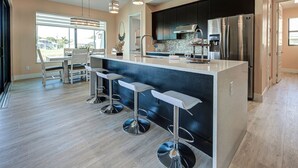 Une cuisine moderne dotée d’un îlot central, d’appareils électroménagers en acier inoxydable et de tabourets de bar.