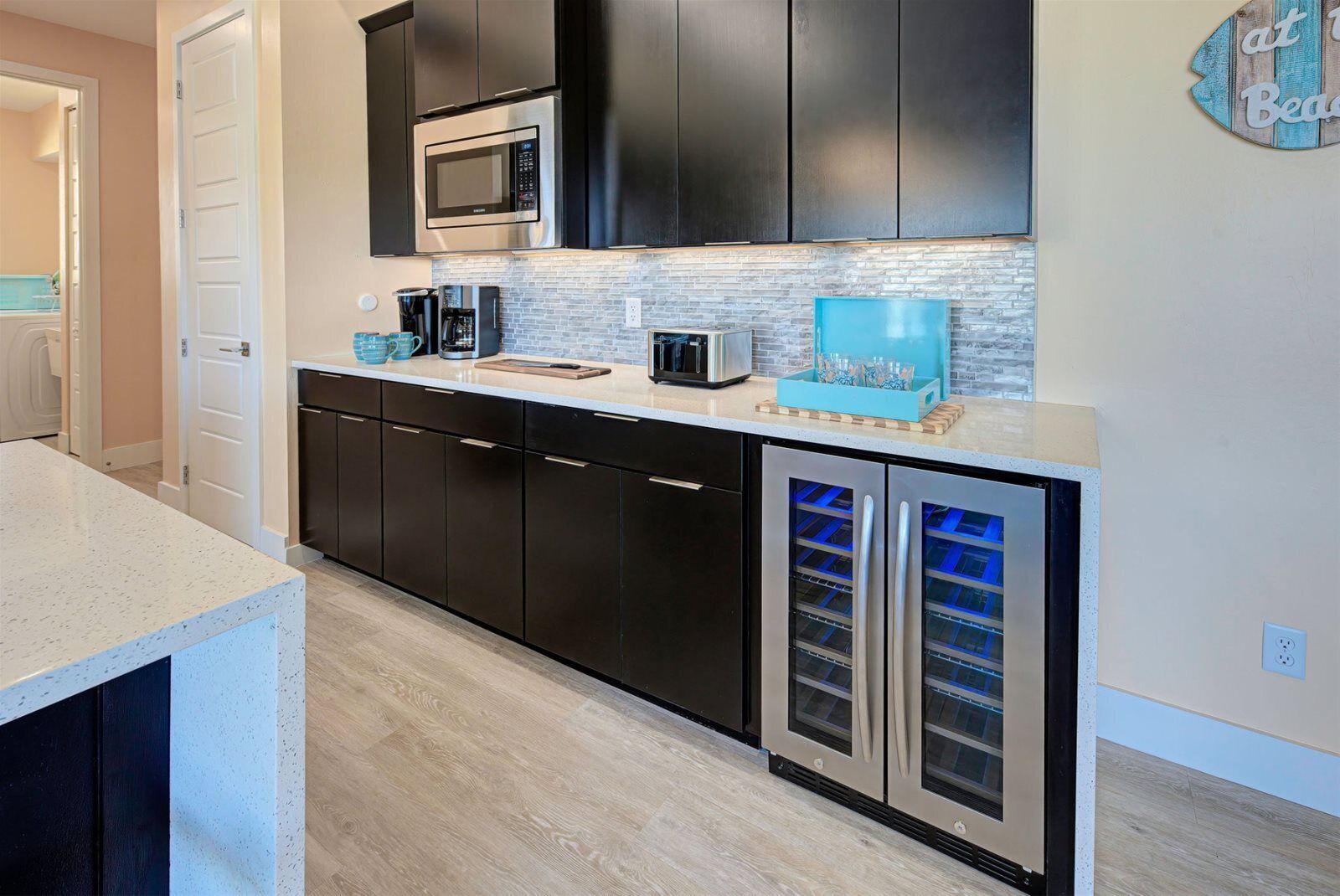 A modern kitchen with dark cabinets, a stainless steel microwave, a coffee maker, and a built-in wine cooler.