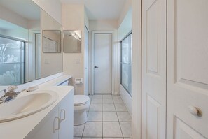 A narrow, white bathroom with a sink, toilet, and a door leading to another room. - Endless Summer (Port Charlotte)