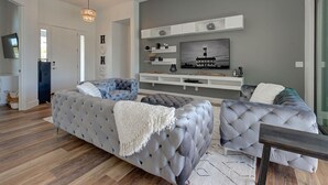 Una sala de estar moderna con un sofá gris, un televisor de pantalla plana montado en un estante blanco y suelo de madera.