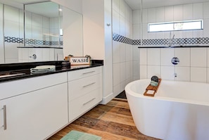 Un baño moderno con muebles blancos, encimera negra y una bañera independiente.