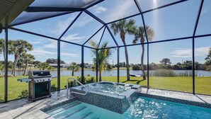 Zona de piscina con jacuzzi, parrilla y vistas a un lago y palmeras.