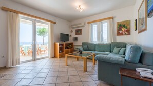 A living room with a sofa, a coffee table, a TV, and a sliding glass door leading to an outdoor area. - Villa Adamite (4 bedrooms) (Lavrio)