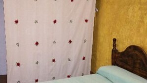 A room with a bed, a curtain with a floral pattern, and a wooden headboard.