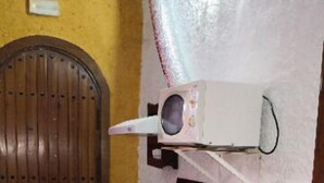 A small kitchen with a wooden door, a microwave, a bowl on the counter, and a trash bin.