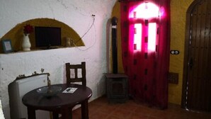 A room with a dining table, chairs, a small TV on the wall, a red door, and a wooden door.