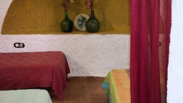 A small, cozy room with a single bed, a bench, and a shelf with decorative items.