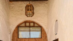 A corridor with a wooden door at the end, a white chair, and a hanging lantern.