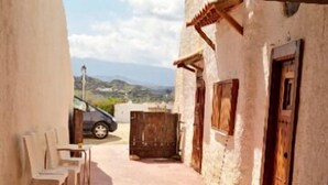 A narrow alleyway with a rustic building, a wooden door, and a view of a car and distant landscape.