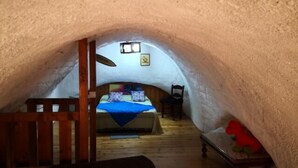 An arched, insulated room with a bed, wooden floor, and a small table with a red object.