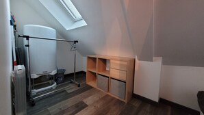Una habitación pequeña con tragaluces, un carrito metálico y un mueble de madera con cajones.