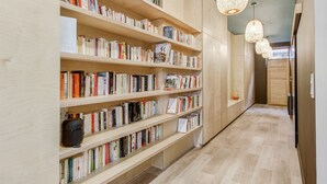 Et bibliotek med flere træbogreoler fyldt med bøger, trægulv og hængende lysarmaturer.