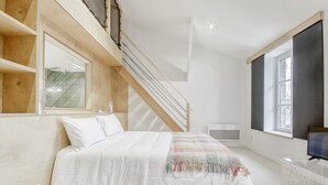 Et moderne soveværelse med seng, trætrappe, stort vindue og et fjernsyn.