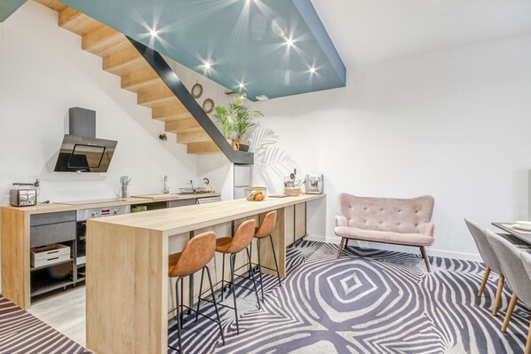 Una cocina moderna con una isla de madera, taburetes de bar y una escalera con techo azul.