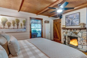 A bedroom with a bed, a stone fireplace, a ceiling fan, and a door with a window.