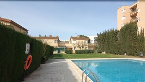 A swimming pool with a lifebuoy, surrounded by neatly trimmed hedges and residential buildings. - Charming house for rent in Roses, Costa Brava! 1200 meters from the beach. Large terrace and community pool. (Roses)
