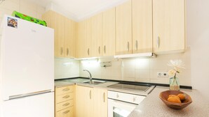 A kitchen with wooden cabinets, a white refrigerator, a sink, and a countertop with a bowl of fruit and a vase with flowers. - Charming house for rent in Roses, Costa Brava! 1200 meters from the beach. Large terrace and community pool. (Roses)