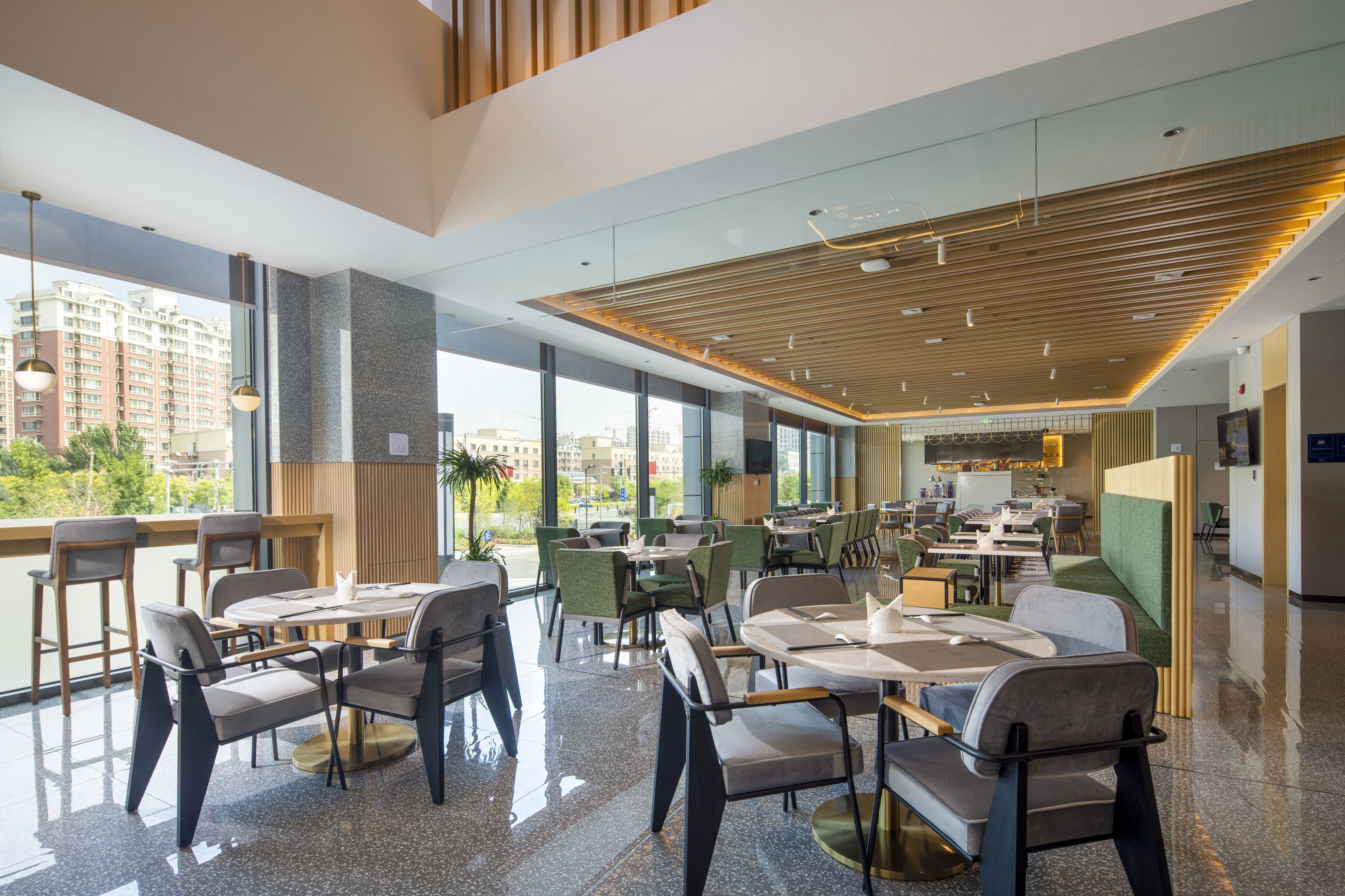 Un restaurante moderno con techos altos, ventanas amplias y una variedad de opciones de asientos, incluyendo mesas y cabinas.