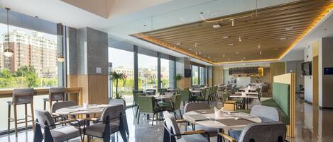 En modern restaurang med högt i tak, stora fönster och en variation av sittplatser, inklusive bord och avskilda sittgrupper.