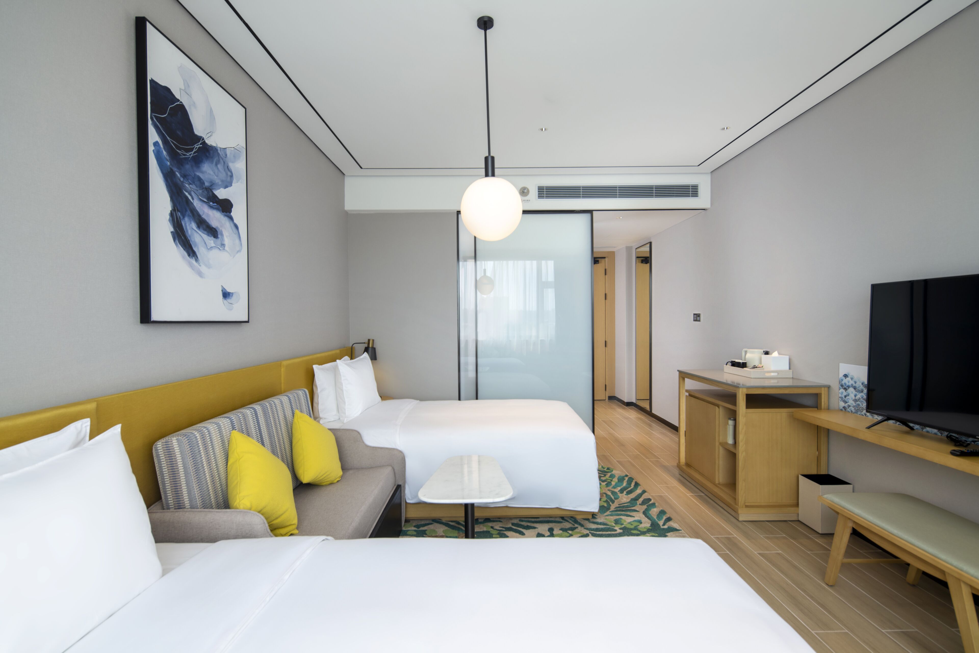A hotel room with two beds, a sofa, a small table, a TV, and a painting on the wall.