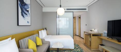 A hotel room with two beds, a sofa, a small table, a TV, and a painting on the wall.