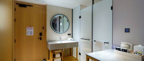 Een moderne badkamer met een houten deur, een ronde spiegel, een wastafel en een tafel met toiletartikelen.