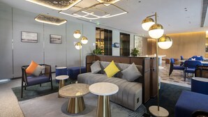 A modern hotel lobby with a sofa, chairs, and tables, featuring geometric ceiling designs and ambient lighting. - Hilton Garden Inn Changchun Economic Development Zone (Changchun)
