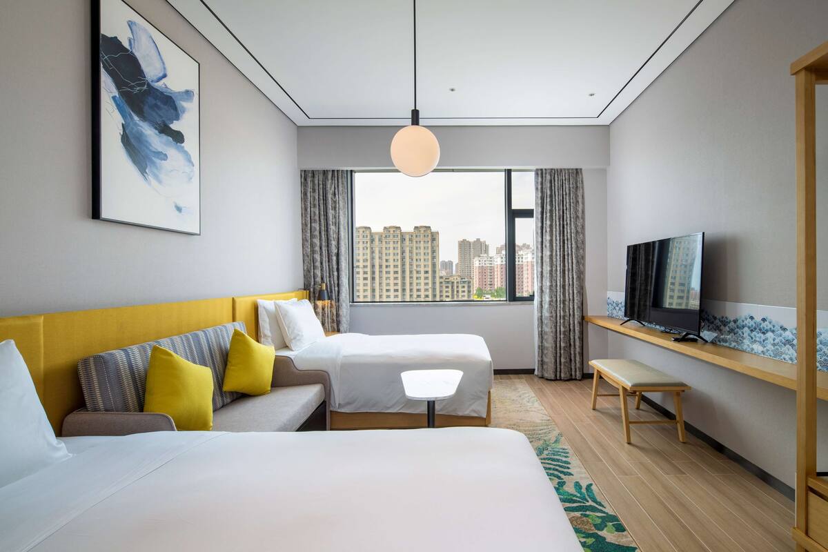 A hotel room with two beds, a TV, and a city view.