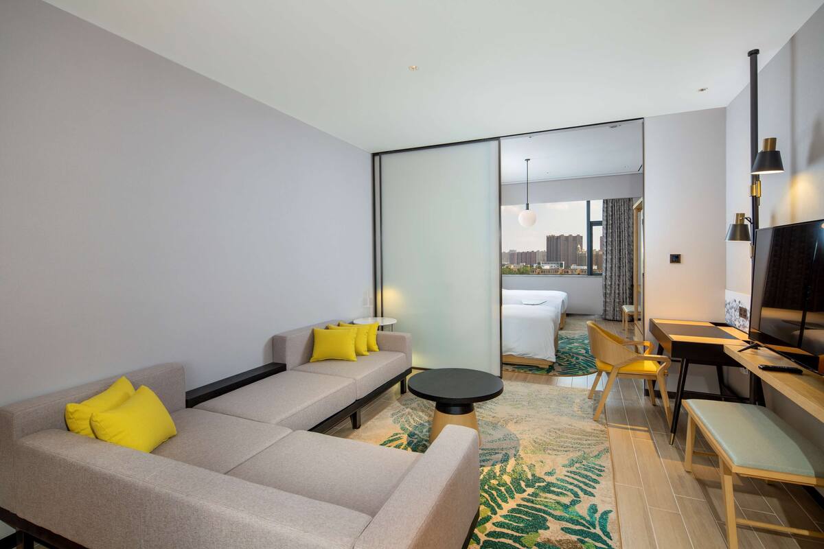 A modern hotel room with a sofa, a dining table, and a TV.