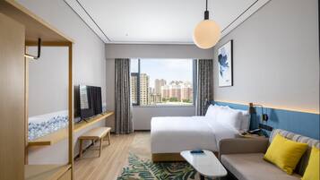 A hotel room with a bed, a sofa, a TV, a desk, and a window with a city view.