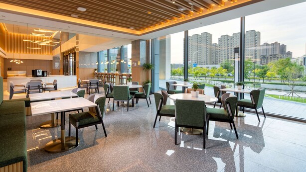 A modern restaurant with a high ceiling, large windows, and a view of a cityscape. - Hilton Garden Inn Changchun Economic Development Zone (Changchun)