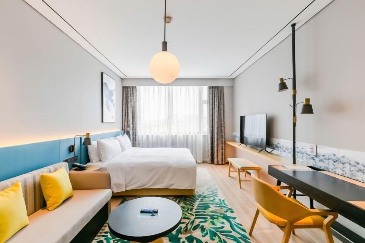 Quarto de hotel com uma cama, um sofá, uma escrivaninha, uma cadeira e uma televisão.