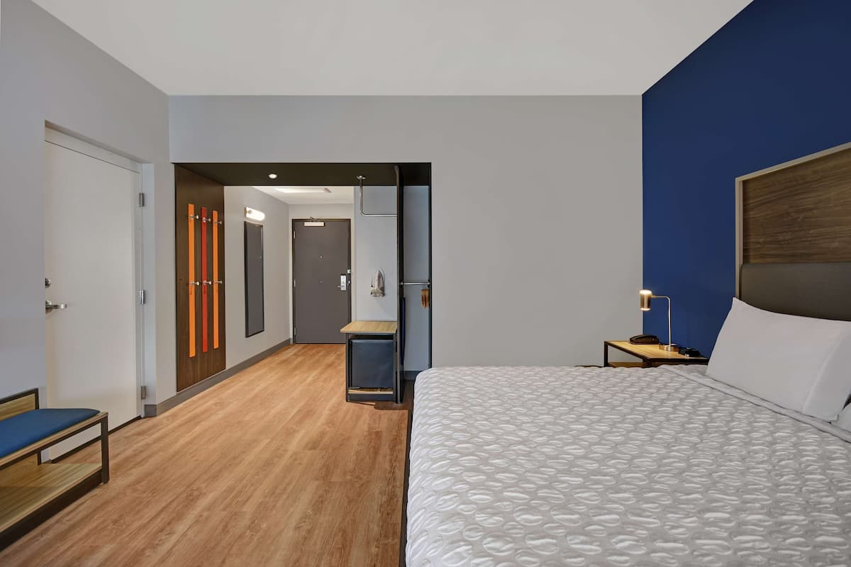 A modern hotel room with a large bed, a desk, and a small seating area.