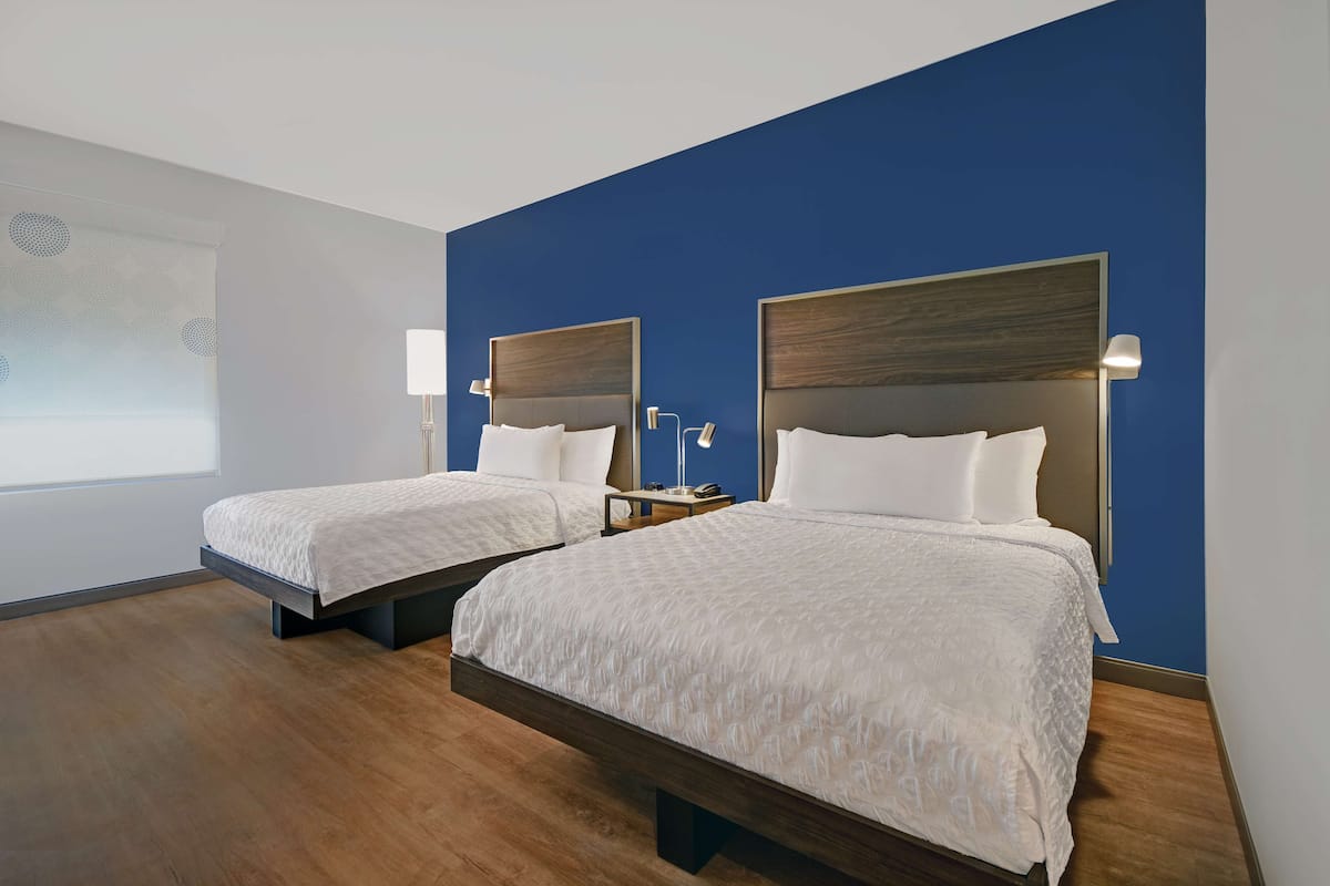 A hotel room with two beds, a blue accent wall, and a large window.