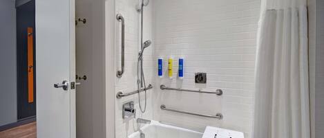 A modern bathroom with a white bathtub, grab bars, and a shower with a handheld showerhead.