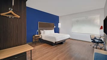 A modern hotel room with a bed, bedside table, chair, and a desk with a chair.