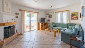 A living room with a sofa, coffee table, fireplace, television, and a view to the outside. - Villa Adamite (2 bedrooms) (Lavrio)