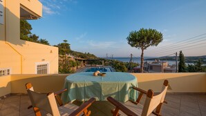A round table with a green tablecloth and wooden chairs on a balcony overlooking a swimming pool and a scenic view of the sea and hills. - Villa Adamite (2 bedrooms) (Lavrio)