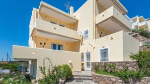 A multi-story building with balconies, a stone wall, and a clear blue sky. - Villa Adamite (2 bedrooms) (Lavrio)
