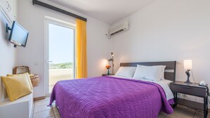 A bedroom with a large bed, a nightstand, a TV, and a window with curtains. - Villa Adamite (2 bedrooms) (Lavrio)