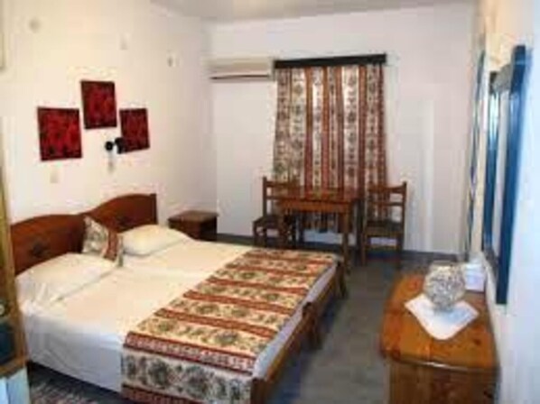 A bedroom with a bed, a wooden chair, a small table, and a wall-mounted air conditioning unit. - Captivating 1-bed Apartment in Lefkos (Karpathos)