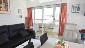 Una sala de estar moderna con un sofá de cuero negro, una mesa de comedor blanca con un jarrón de flores y un sillón gris.