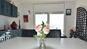 Un comedor con una mesa, sillas, un jarrón con flores, un armario azul y vistas al exterior por una ventana.